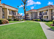 Thumbnail 12 of 23 - A sunny day at a well-kept apartment complex with green lawns and clear skies.