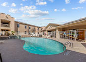 Thumbnail 13 of 18 - A swimming pool in front of a building with a blue sky and clouds in the background.