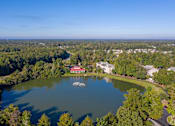 Thumbnail 46 of 50 - A serene lake surrounded by lush greenery and a few buildings in the distance.