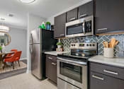 Thumbnail 1 of 44 - A modern kitchen with a stainless steel refrigerator, microwave, oven, and a tile backsplash.