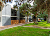 Thumbnail 24 of 28 - A building with a red door and a balcony is surrounded by trees and a picnic table.