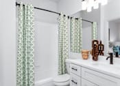 Thumbnail 14 of 50 - A bathroom with a toilet, sink, and green patterned shower curtains.