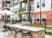 Thumbnail 6 of 43 - A patio with a bar and chairs in front of a building.