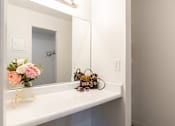 Thumbnail 11 of 28 - A white bathroom vanity with a mirror, a vase with flowers, a bicycle, and a pair of sunglasses.