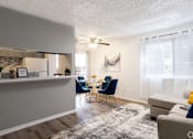 Thumbnail 4 of 28 - A living room with a grey couch and a dining table with blue chairs.