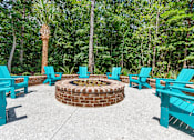 Thumbnail 21 of 50 - A fire pit surrounded by blue chairs in a forest setting.