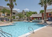 Thumbnail 19 of 32 - A swimming pool surrounded by palm trees and residential buildings.