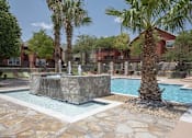 Thumbnail 21 of 32 - A pool with a waterfall and a palm tree in front of a red building.