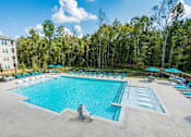 Thumbnail 19 of 31 - A large outdoor swimming pool surrounded by trees and lounge chairs.
