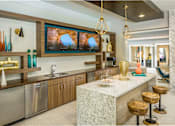Thumbnail 5 of 31 - A modern kitchen in clubroom with stools and large televisions.