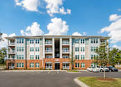 Thumbnail 30 of 31 - A large apartment building with a parking lot in front.