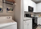 Thumbnail 6 of 41 - A white washing machine is in a kitchen with white cabinets.