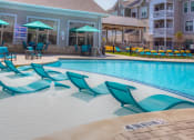 Thumbnail 22 of 34 - a swimming pool with blue chaise lounge chairs and umbrellas