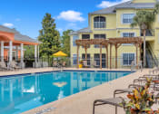 Thumbnail 22 of 35 - Pool with chaise lounges and pergola at Bermuda Estates Apartments in Ormond Beach, FL