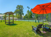 Thumbnail 21 of 25 - two benches and an umbrella in the grass near a tennis court