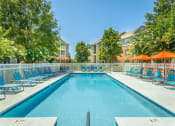 Thumbnail 19 of 25 - a swimming pool with blue chairs and orange umbrellas in front of a building