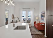Thumbnail 9 of 55 - A modern kitchen with a white countertop and a stainless steel sink and a goose neck faucet, with bright natural lights and glass patio doors.