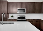 Thumbnail 43 of 55 - A modern kitchen with amble storage with a white countertop and dark brown cabinets.