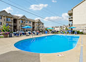 Thumbnail 17 of 21 - A swimming pool surrounded by chairs and umbrellas in front of apartment buildings.