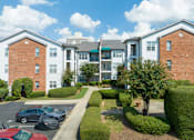 Thumbnail 4 of 19 - A large apartment complex with a parking lot in front.