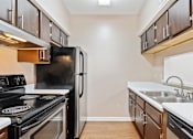 Thumbnail 13 of 19 - A kitchen with a black refrigerator, stove, and wooden cabinets.