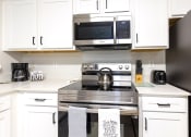 Thumbnail 4 of 25 - a kitchen with white cabinets and a stove and a microwave