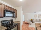 Thumbnail 4 of 34 - a kitchen with a stove and microwave and a living room with a couch at 10X Audubon Park apartments in Daphne, AL 