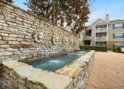 Thumbnail 28 of 34 - a stone wall with a fountain in front of a house at 10X Audubon Park apartments in Daphne, AL 