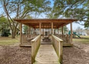 Thumbnail 25 of 34 - a small wooden bridge leading to a cabin with a playground in the background at 10X Audubon Park apartments in Daphne, AL 