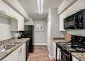 Thumbnail 4 of 26 - Kitchen with white cabinets and black appliances  at Mirabelle Apartments in Mobile, Alabama