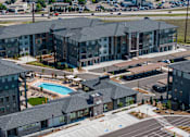 Thumbnail 29 of 58 - A large apartment complex with a pool and a parking lot.