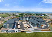Thumbnail 28 of 58 - A large, modern building complex with a parking lot in front.