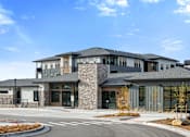 Thumbnail 26 of 58 - A modern building with a stone facade and a curved driveway in front.
