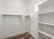 Thumbnail 25 of 29 - a spacious walk in closet with white walls and wood flooring