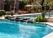 Thumbnail 4 of 26 - Water flowing over water feature from heated lap pool into second pool area surrounded by lush mature landscaping and poolside seating