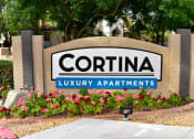 Thumbnail 9 of 26 - Signage reading Cortina Luxury Apartments with orange and red flowers planted in garden in front of sign