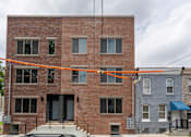 Thumbnail 1 of 8 - A red brick building with a grey door and windows.