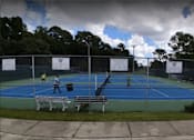 Thumbnail 14 of 14 - A tennis court with people playing tennis and a cloudy sky.