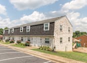Thumbnail 1 of 31 - A white brick building with a black roof and a parking lot in front.
