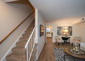 Thumbnail 16 of 31 - A staircase with a white railing leads to a living room with a couch, chairs, and a coffee table.