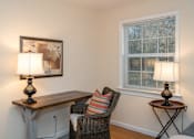 Thumbnail 19 of 31 - A room with a chair and a table with a lamp on it.