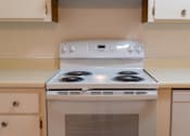Thumbnail 11 of 22 - a white stove top oven in a kitchen with white cabinets at Cowell Terrace Apartments, Concord California