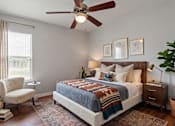 Thumbnail 16 of 23 - A bedroom with a bed, chair, and ceiling fan.