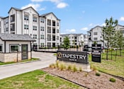 Thumbnail 1 of 19 - A sign for Tapestry Apartments is displayed in front of a building.
