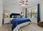 Thumbnail 16 of 27 - A bedroom with a blue bedspread and a ceiling fan.