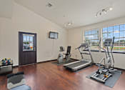 Thumbnail 14 of 23 - A spacious room with a treadmill, exercise bike, and a television.