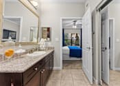 Thumbnail 15 of 27 - A bathroom with a sink, mirror, and a bed in the background.
