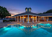 Thumbnail 6 of 23 - A pool in front of a house with lights on.