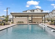 Thumbnail 5 of 40 - A large swimming pool in front of a building with a covered seating area.