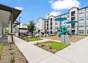 Thumbnail 13 of 19 - A modern apartment complex with a playground and a fence.